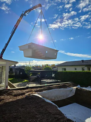 Glasfiberpool lyfts med kran över villaträdgård i motljus