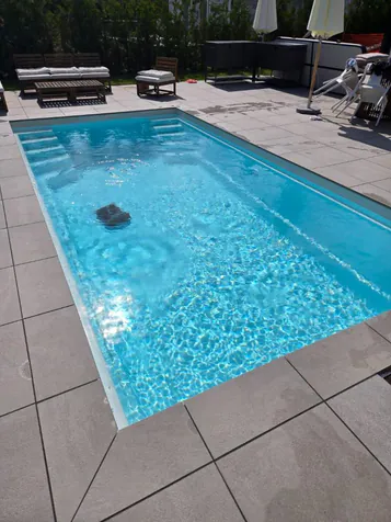 Glasfiberpool med solreflexer i vattnet och grå plattor