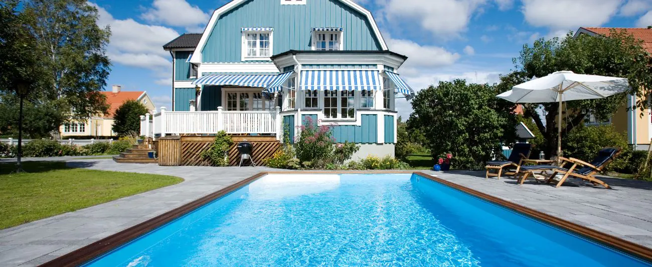 Utomhuspool framför blåvit villa i Östergötland